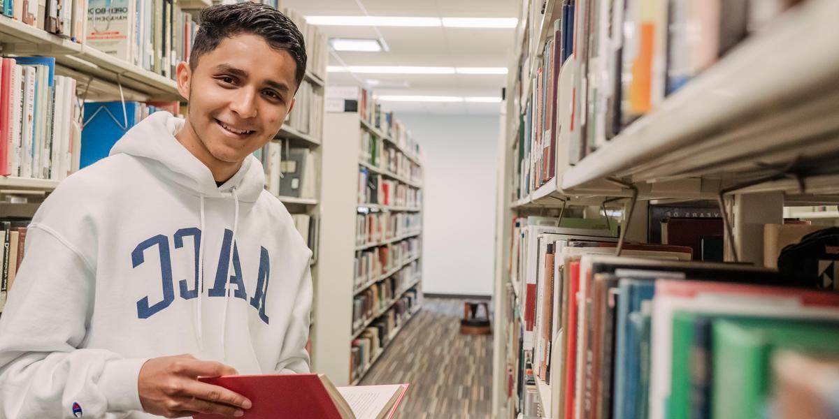 Student smiling for camera with book inside the Truxal Library